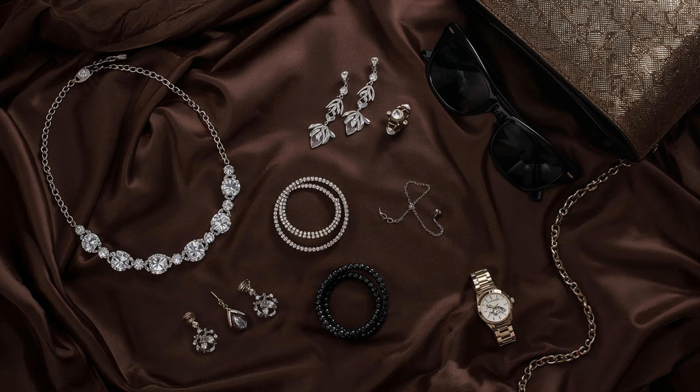 Collection of jewelry including a necklace, earrings, bracelet, and watch on brown fabric.
